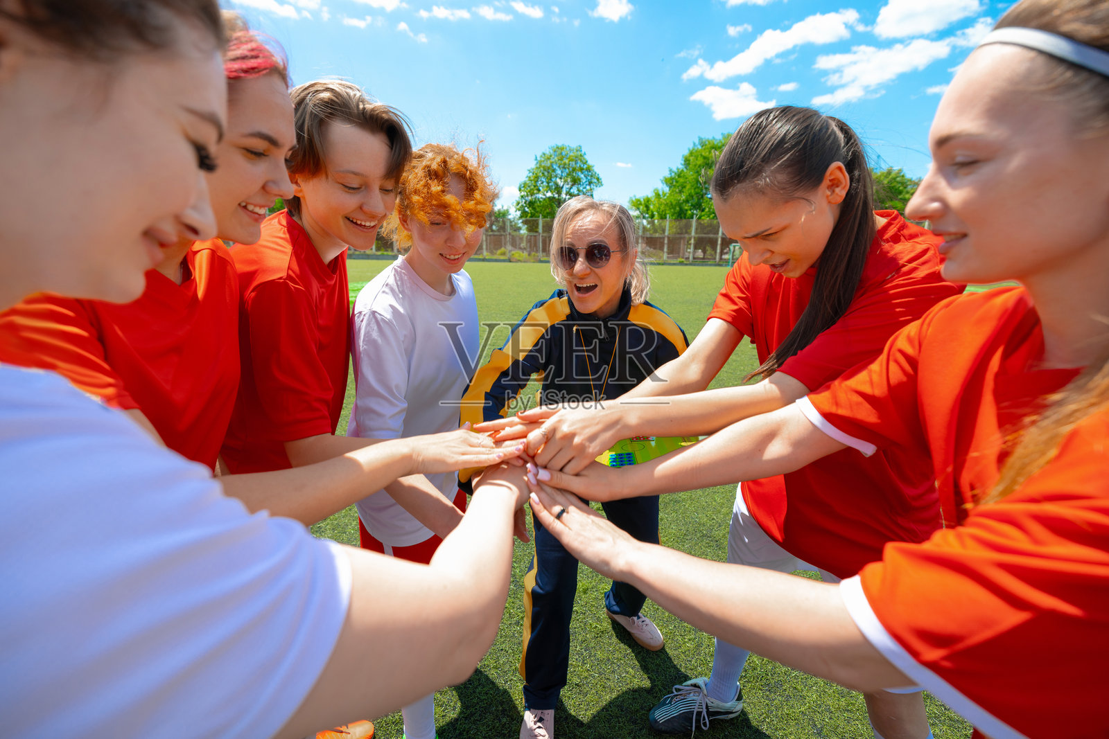 比赛前，女子足球队队员和女教练在阳光明媚的球场上围成一圈，手牵着手。照片摄影图片