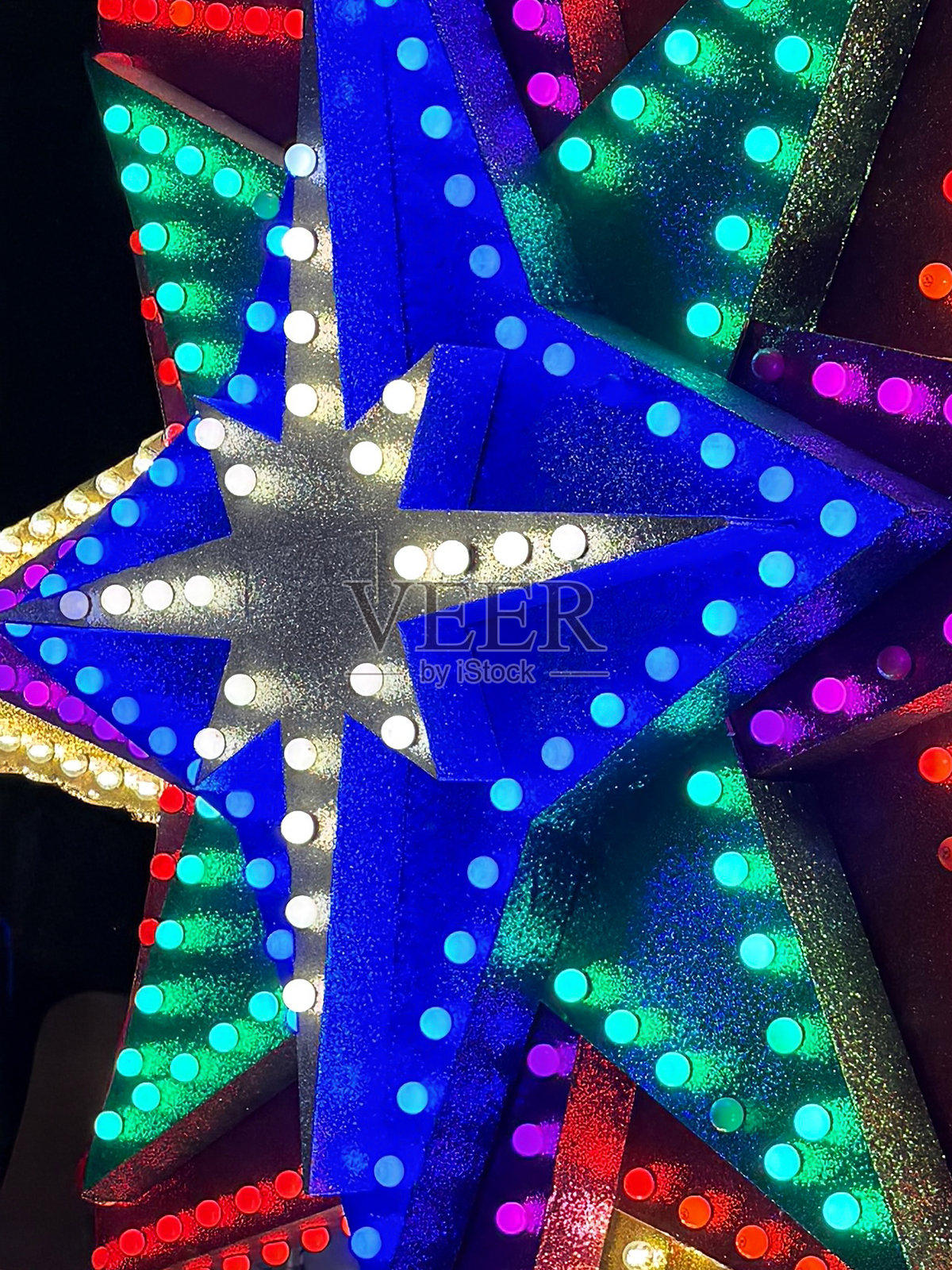 全画幅图像，展示室内公共季节性展示背景下，前景聚焦的彩色、闪光粉覆盖的星星设计的发光仙女灯。照片摄影图片