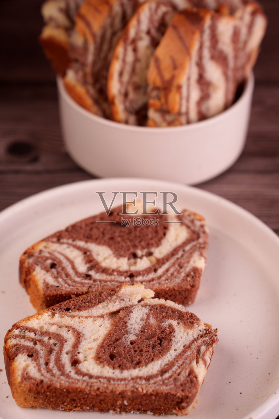 白色盘子上新鲜切开的大理石纹蛋糕特写，带有微妙的巧克力和香草漩涡图案，在温暖灯光下置于木质背景前，诱人，吸引人，自制照片摄影图片