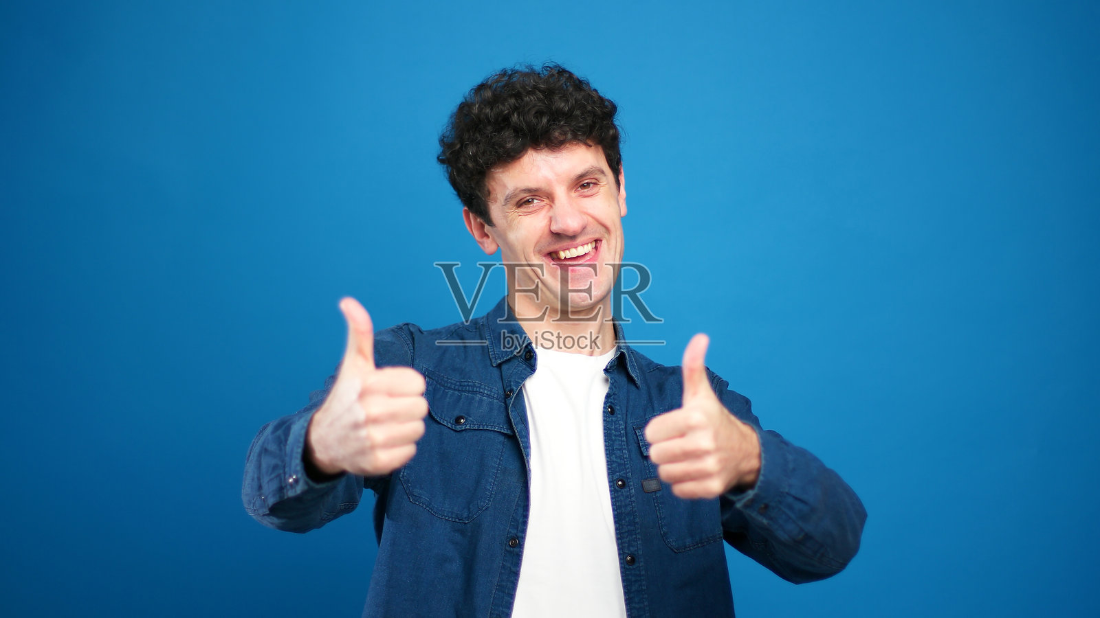 肖像：一位面带微笑、英俊的男士看向镜头，竖起大拇指，背景为蓝色照片摄影图片