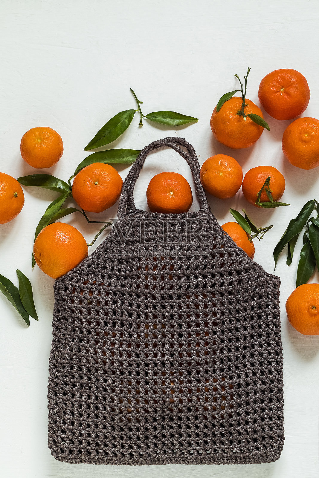白色背景上，一个可重复使用的钩针编织袋里装着充满活力的橙色橘子和新鲜的绿叶，强调天然新鲜和健康饮食。留有复制空间。照片摄影图片