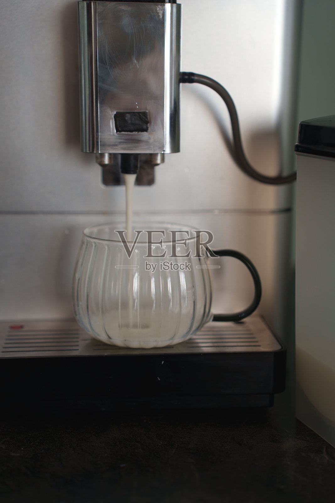 优雅的肋纹玻璃马克杯在时尚的厨房台面上，咖啡机正在倒入液体，特写镜头展示了现代家电设计和温暖的灯光氛围，仪式感，优雅，工业风照片摄影图片