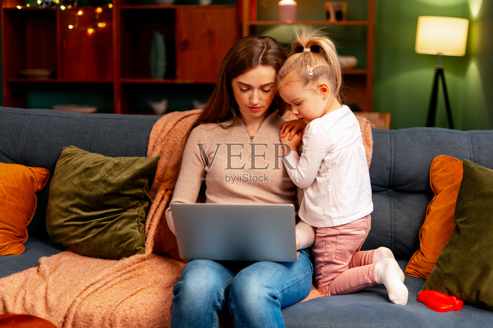 母亲在家用笔记本电脑工作，小女儿在身后观看照片摄影图片