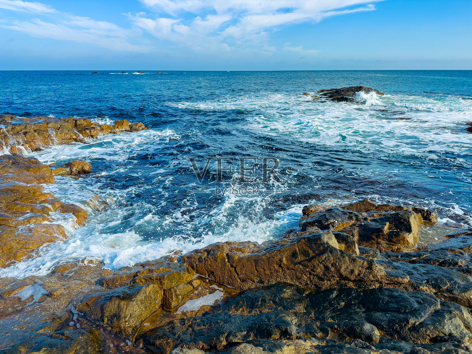 白天，海浪拍打着岩石海岸，远处是蔚蓝的海洋和晴朗的天空，靠近海岸区域照片摄影图片