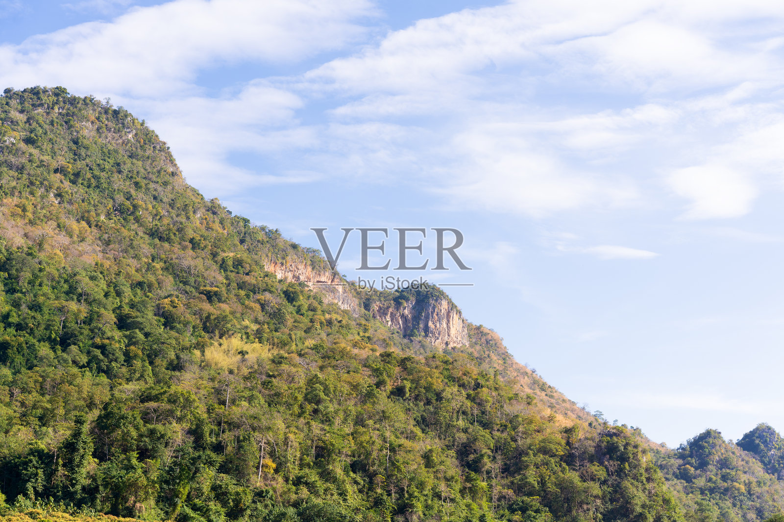 翠绿的山坡上覆盖着茂密的原始森林，天空湛蓝，白云朵朵。风景优美的自然景观，以巨大的岩石悬崖和充满活力的秋叶点缀为特色。照片摄影图片