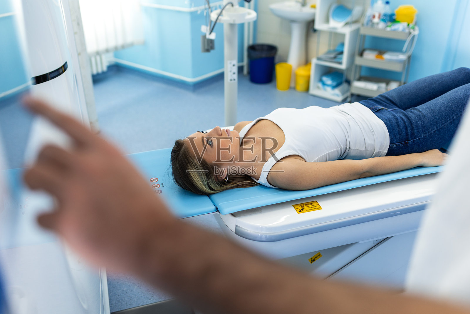 年轻的女患者躺在CT扫描仪的床上，一名医务人员正在操作触摸屏控制面板，准备在现代诊所进行诊断成像检查。照片摄影图片