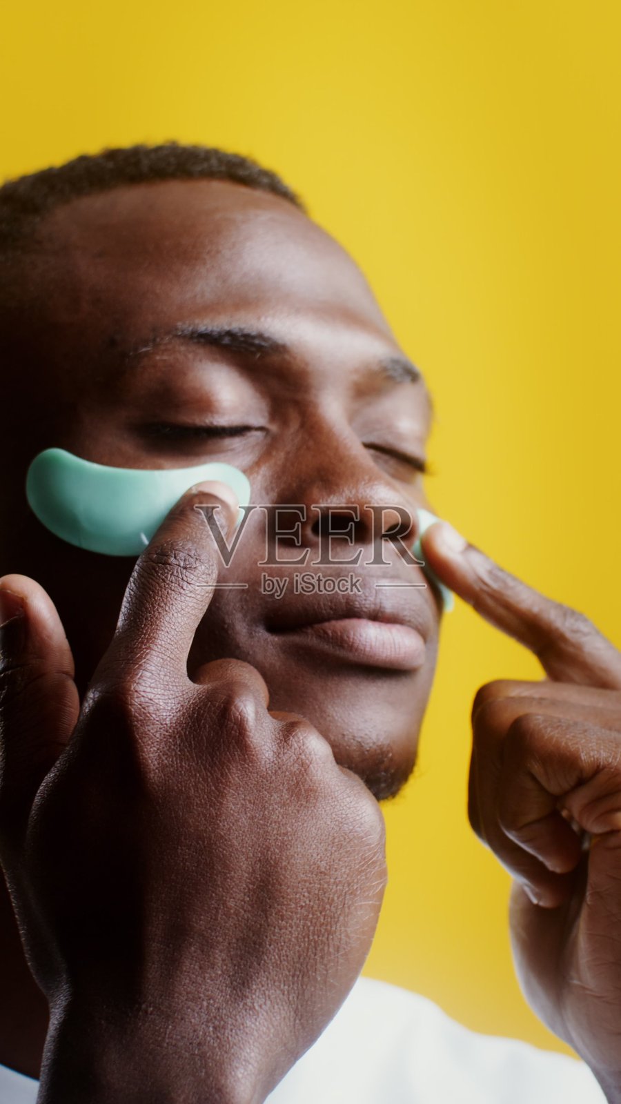 一名男子正在修正在眼下的保湿贴 - 保养。照片摄影图片