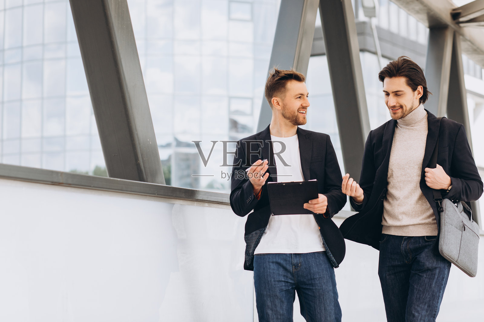 商务伙伴在现代金融区边走边讨论项目想法，手中拿着剪贴板和公文包照片摄影图片