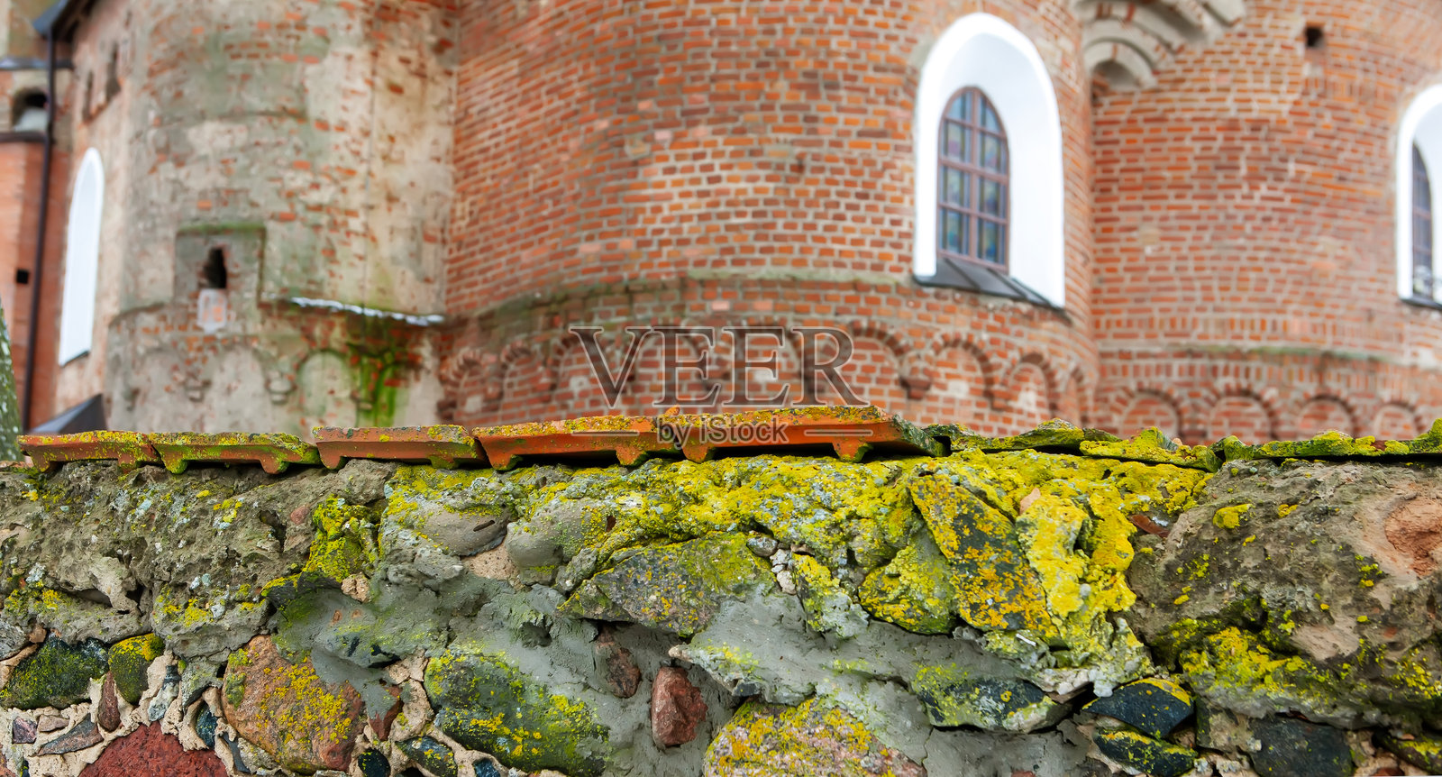 秋季古迹中，覆盖着苔藓和地衣的石墙后矗立着一座古老的砖砌建筑。照片摄影图片