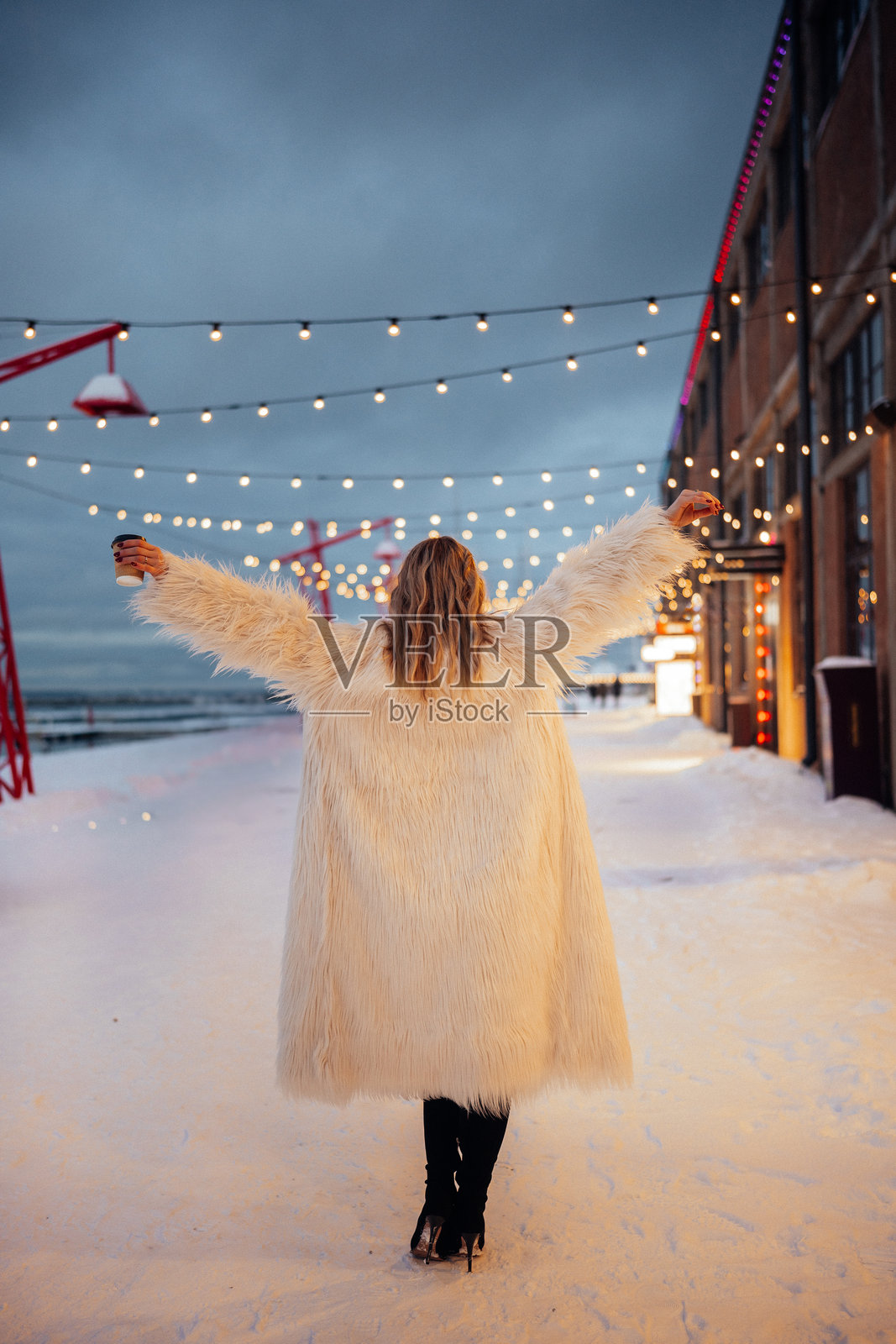 冬日傍晚，女子在海岸边的雪街上，在串灯下行走照片摄影图片