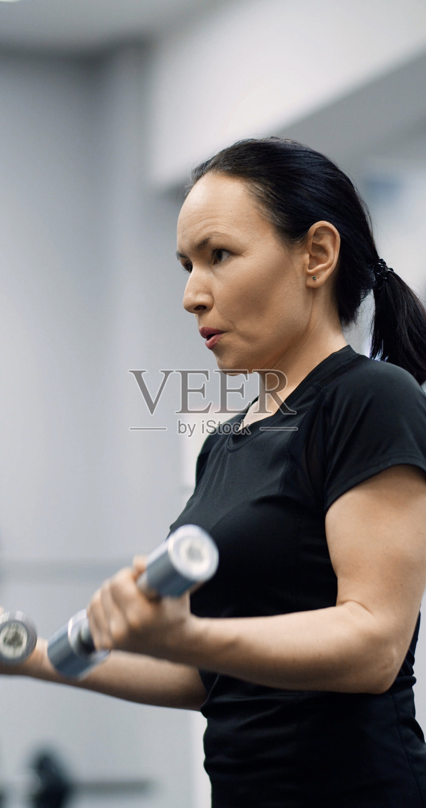 一位健壮的中年女性在进行高强度健身房训练时，使用哑铃锻炼肱二头肌。照片摄影图片