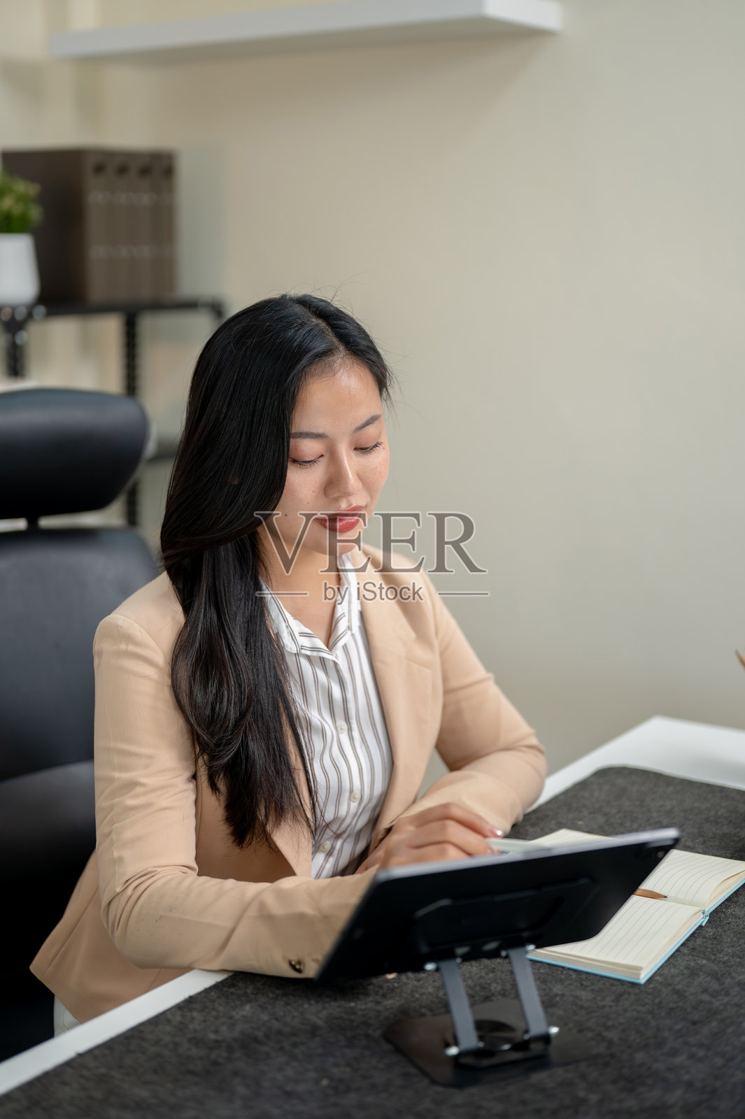 漂亮的亚洲女商人，办公室职员，手持触控笔在桌旁坐着，在平板电脑上书写照片摄影图片