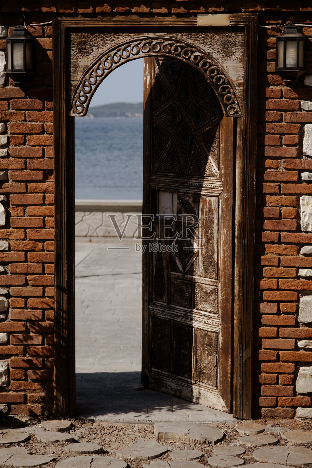 在明亮的夏日阳光下，砖墙上有一个乡村风格的木门，门外是宁静的海景，象征着逃离、自由和新的开始照片摄影图片
