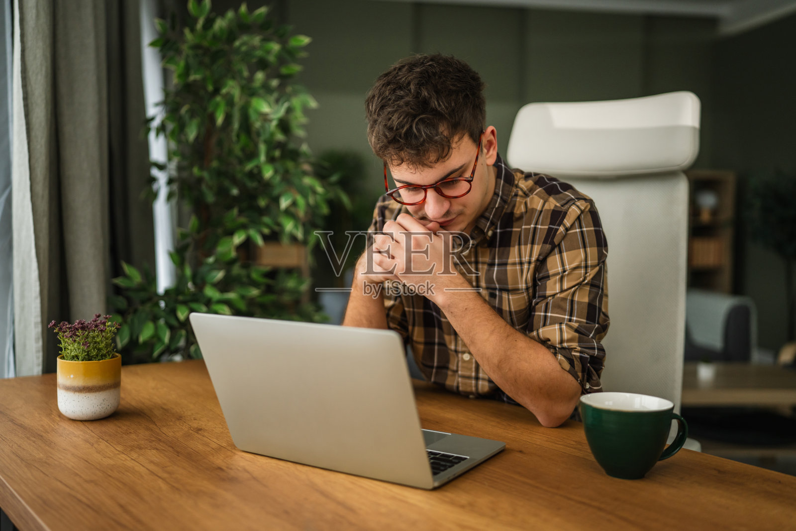 年轻男子在家中的办公室里，一边工作一边思考照片摄影图片