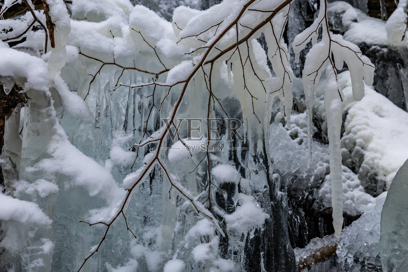 冬日里，冰柱和被雪覆盖的树枝挂在冰冻的岩壁上照片摄影图片