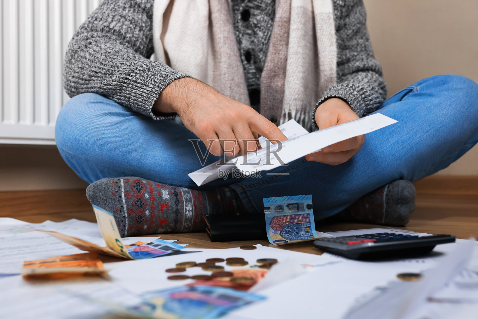 穿着毛衣的男人坐在暖气旁，地板上散落着欧元，他正在计算昂贵的取暖费。照片摄影图片