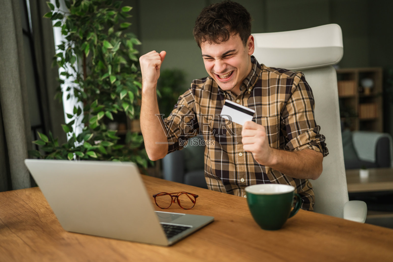 年轻男子用笔记本电脑和信用卡庆祝网上购物成功照片摄影图片