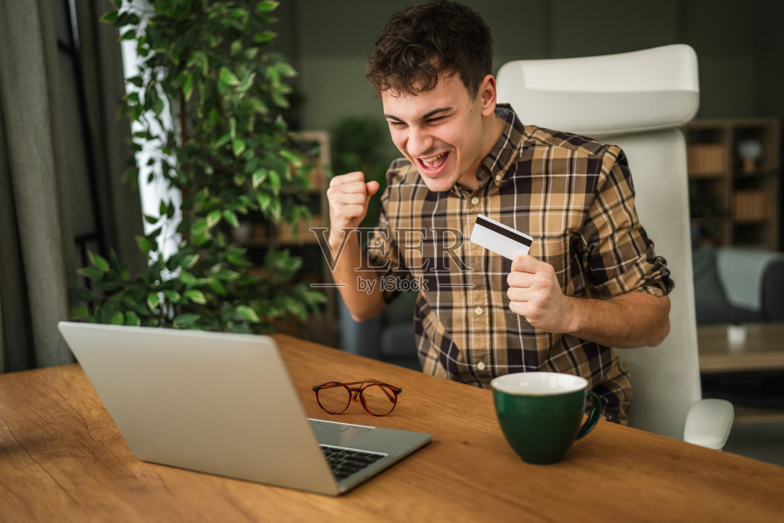 年轻男子用笔记本电脑和信用卡庆祝网上购物成功照片摄影图片