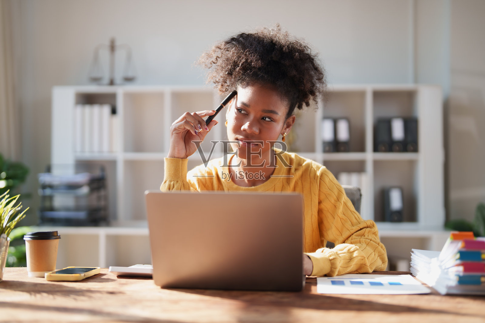 一位年轻的非裔美国女商人坐在办公室的办公桌前，使用笔记本电脑工作，并深入思考，为她的商业项目寻找解决方案照片摄影图片