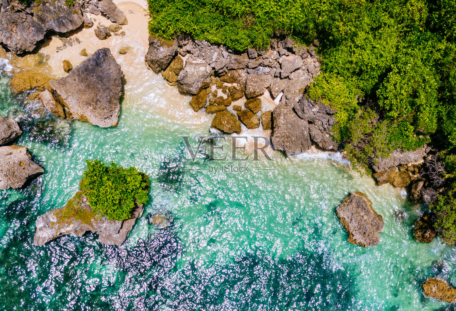从空中俯瞰巴厘岛岩石海岸线，绿植茂盛，清澈碧绿的海水覆盖着珊瑚礁照片摄影图片