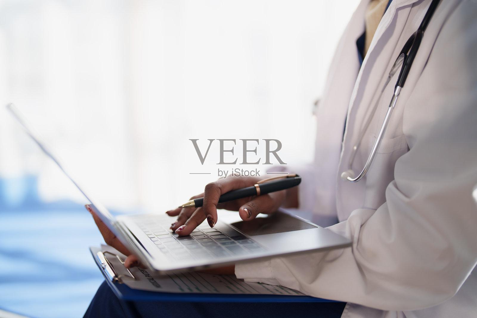 身穿白大褂、戴着听诊器的医护人员正在笔记本电脑上分析医疗数据和患者记录，强调医学中的技术应用照片摄影图片