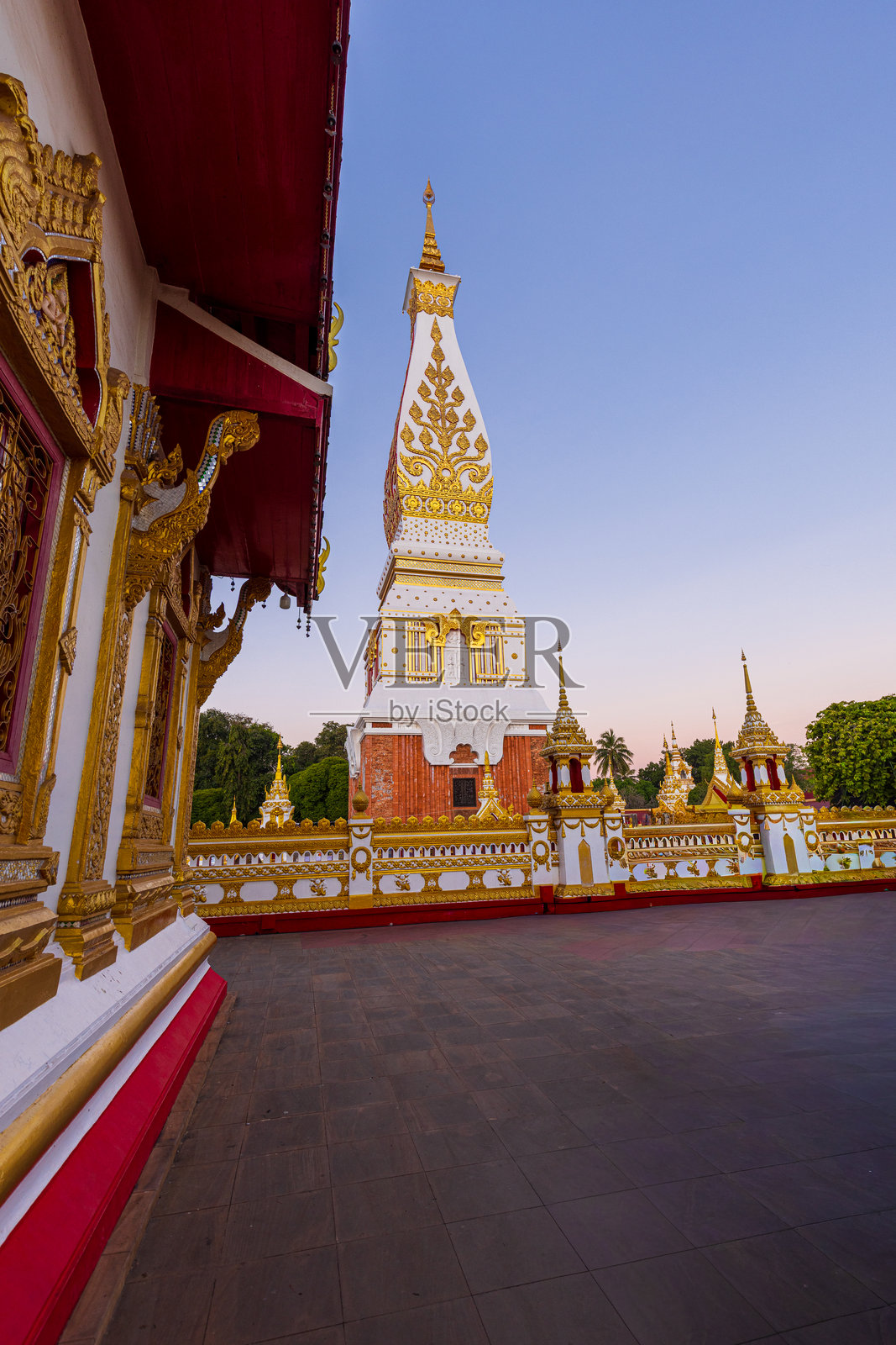 夕阳下，透过华丽的寺庙大门看向佛陀塔，泰国那空帕农府。一张令人惊叹的广角视角，神圣的佛陀塔被精美的金色雕刻寺庙门框所环绕。照片摄影图片