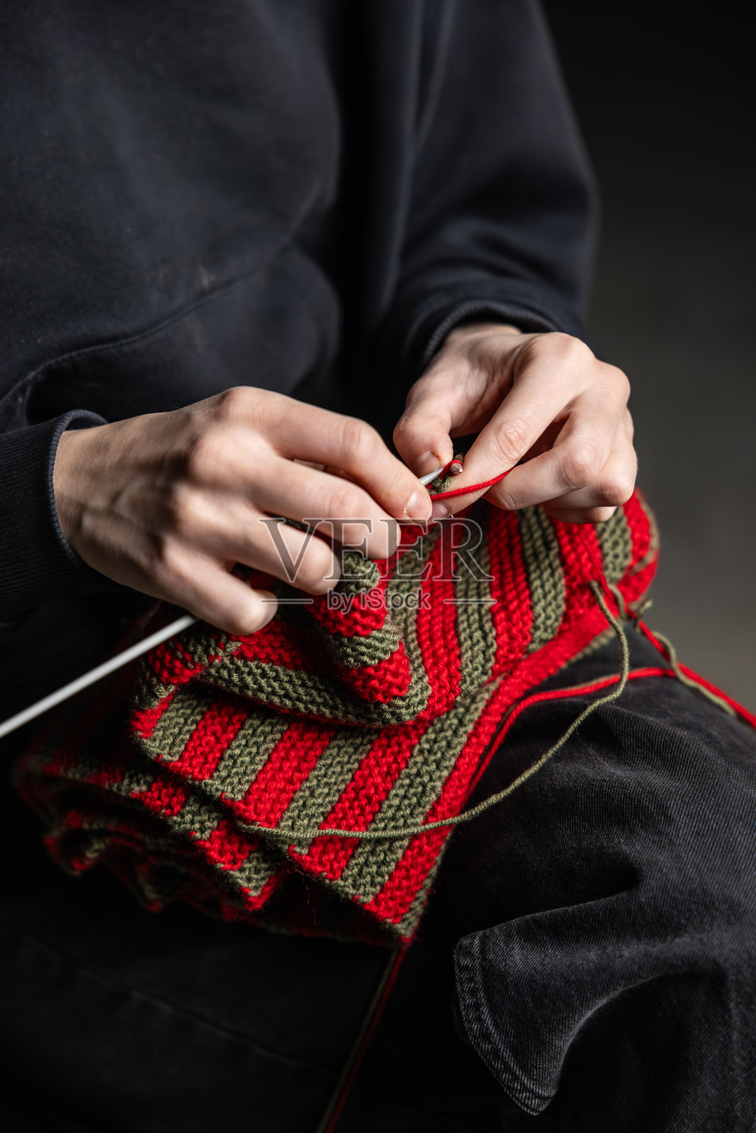 特写：一人正在用红绿线编织条纹织物。此人身着深色衣物，无可见标志或面部。照片摄影图片
