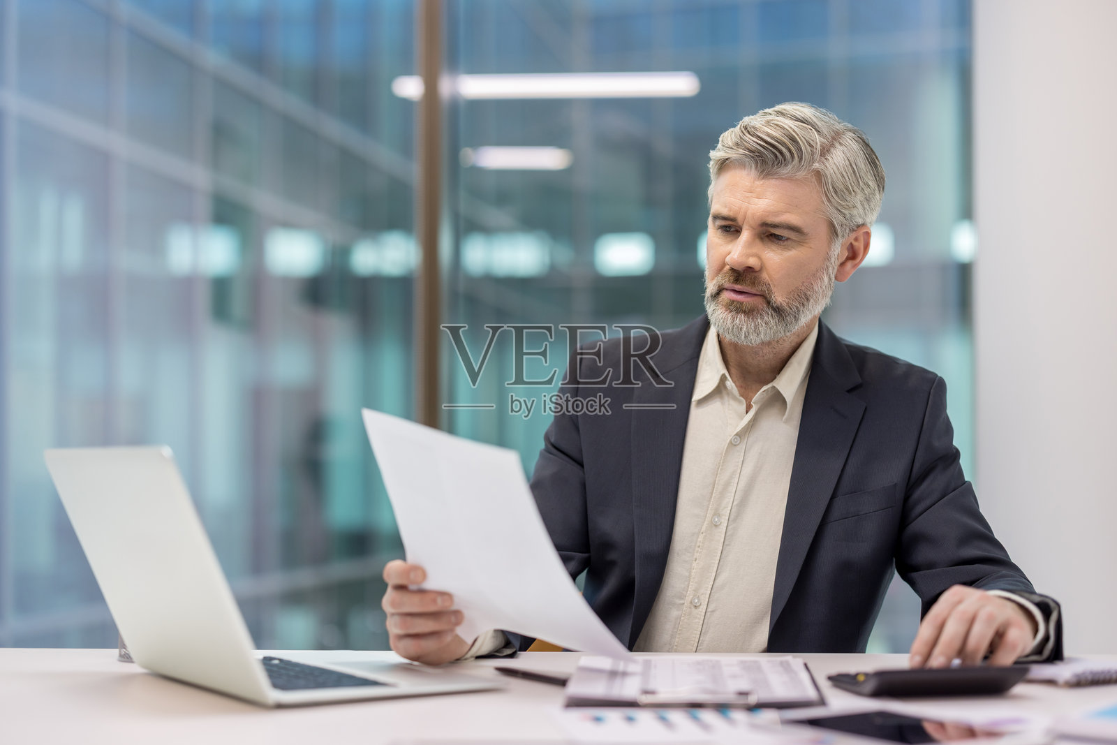 一位成熟的商人在办公室计算预算并审阅财务文件照片摄影图片