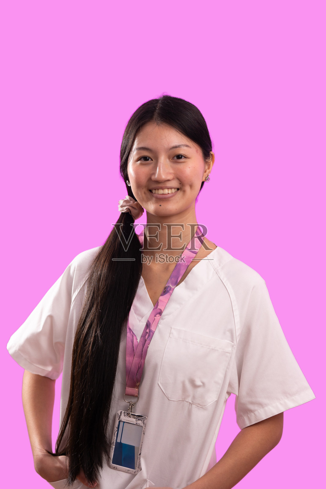 粉色背景上，一位年轻的亚洲女性医护人员微笑着照片摄影图片