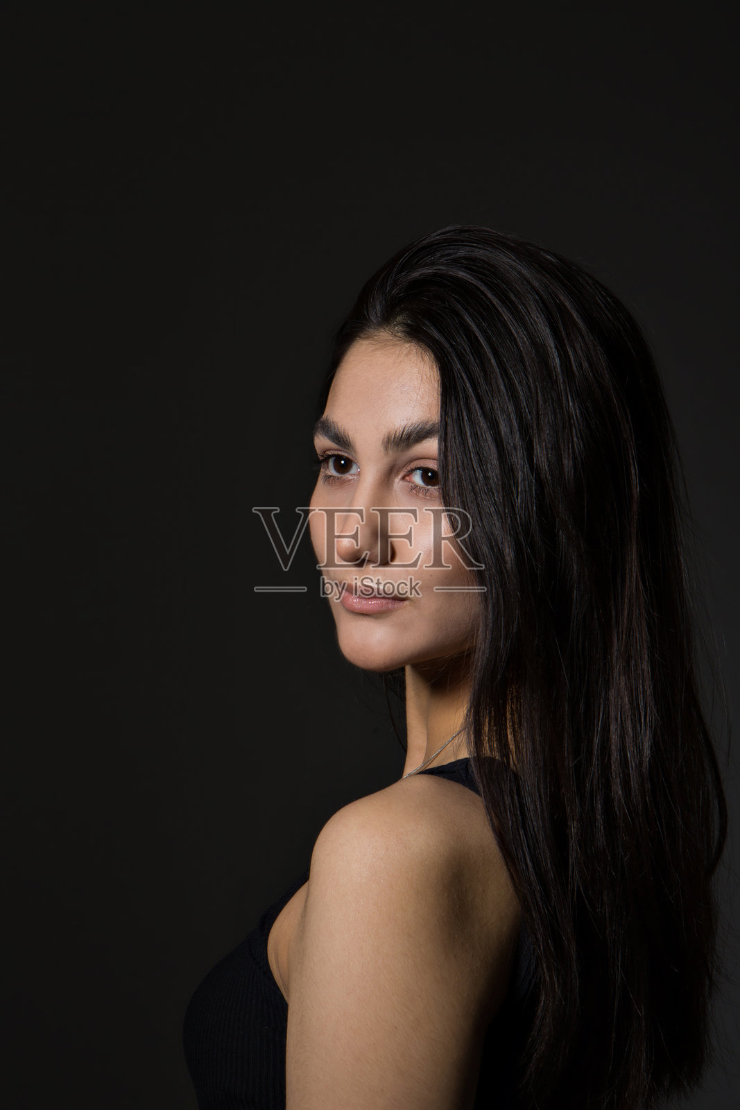 一位黑发女子在早晨醒来，盖着白色毯子，沐浴在阳光中。肖像富有创意，她有着棕色的眼睛。照片摄影图片