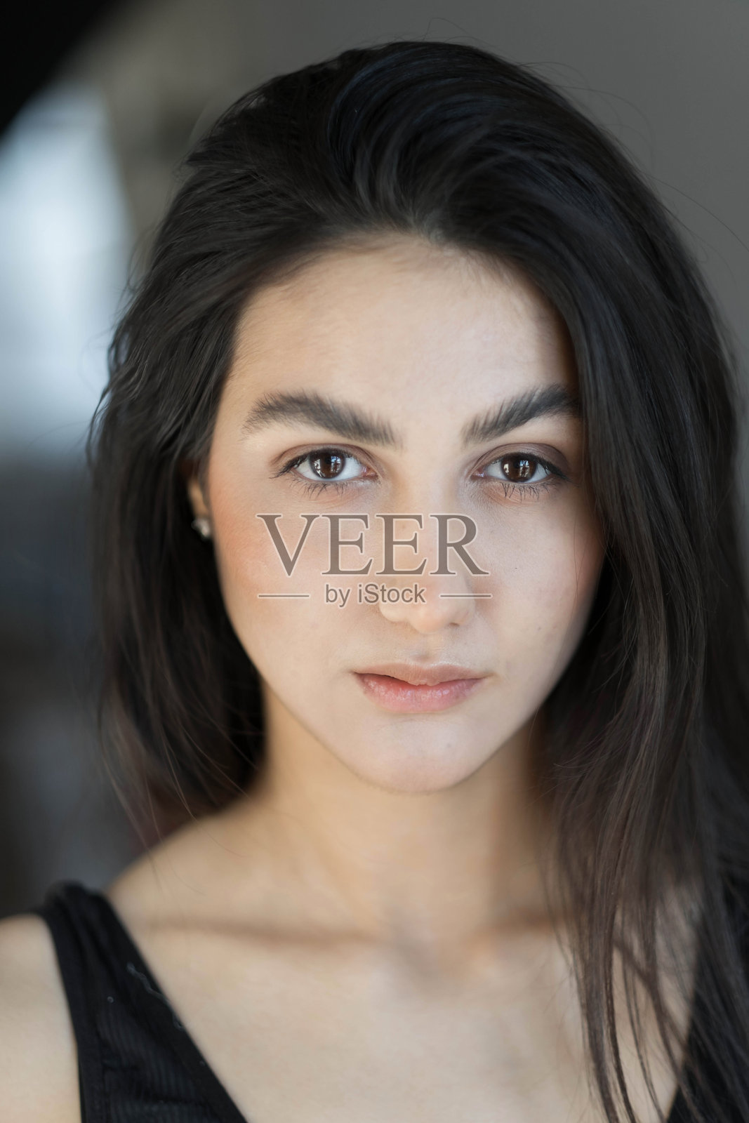 一位黑发女子在早晨从白色毯子中醒来，沐浴着阳光。这幅肖像是创意风格的，她有着棕色的眼睛。照片摄影图片