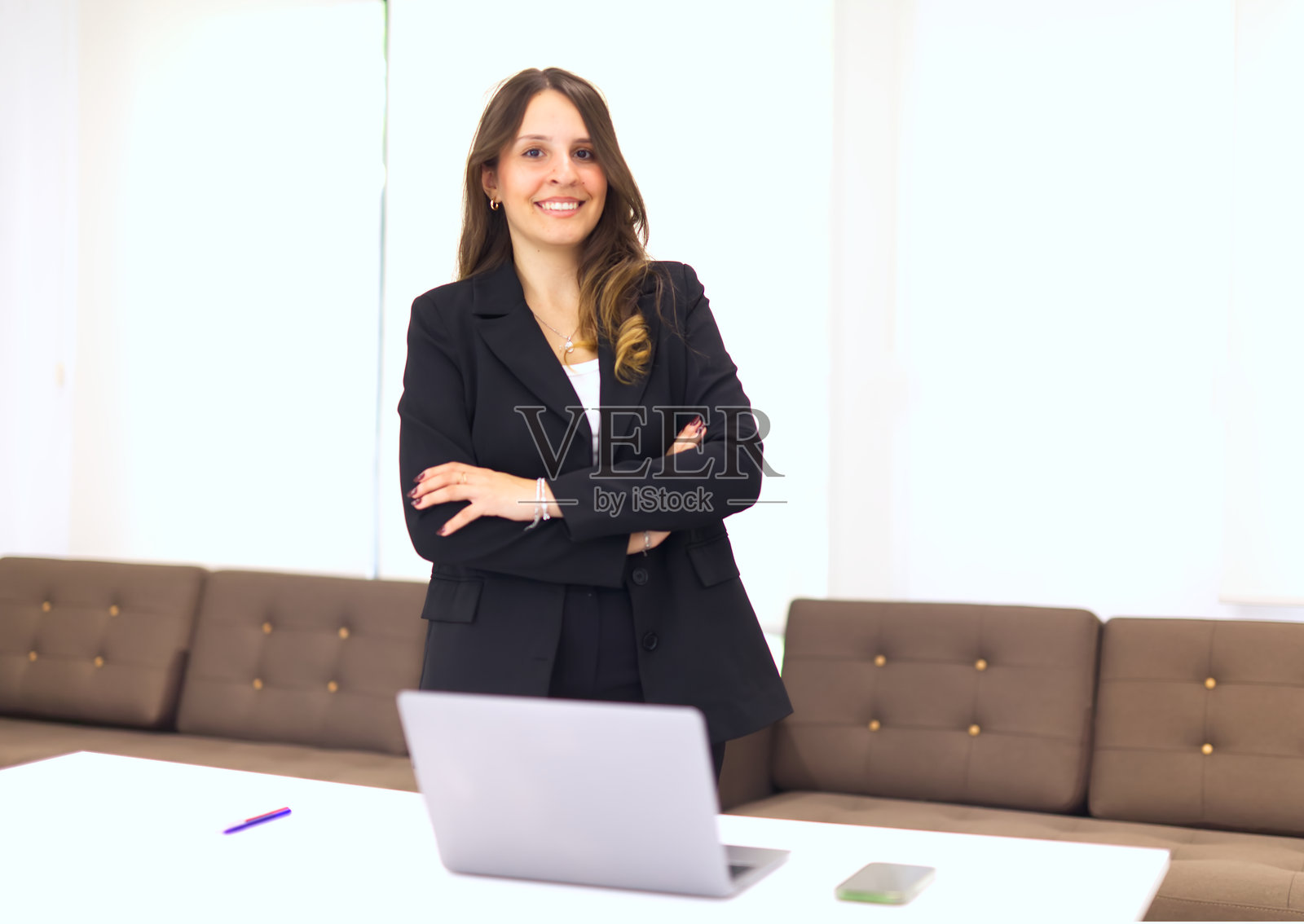 年轻的女商人正在办公室里摆姿势，双臂交叉。照片摄影图片