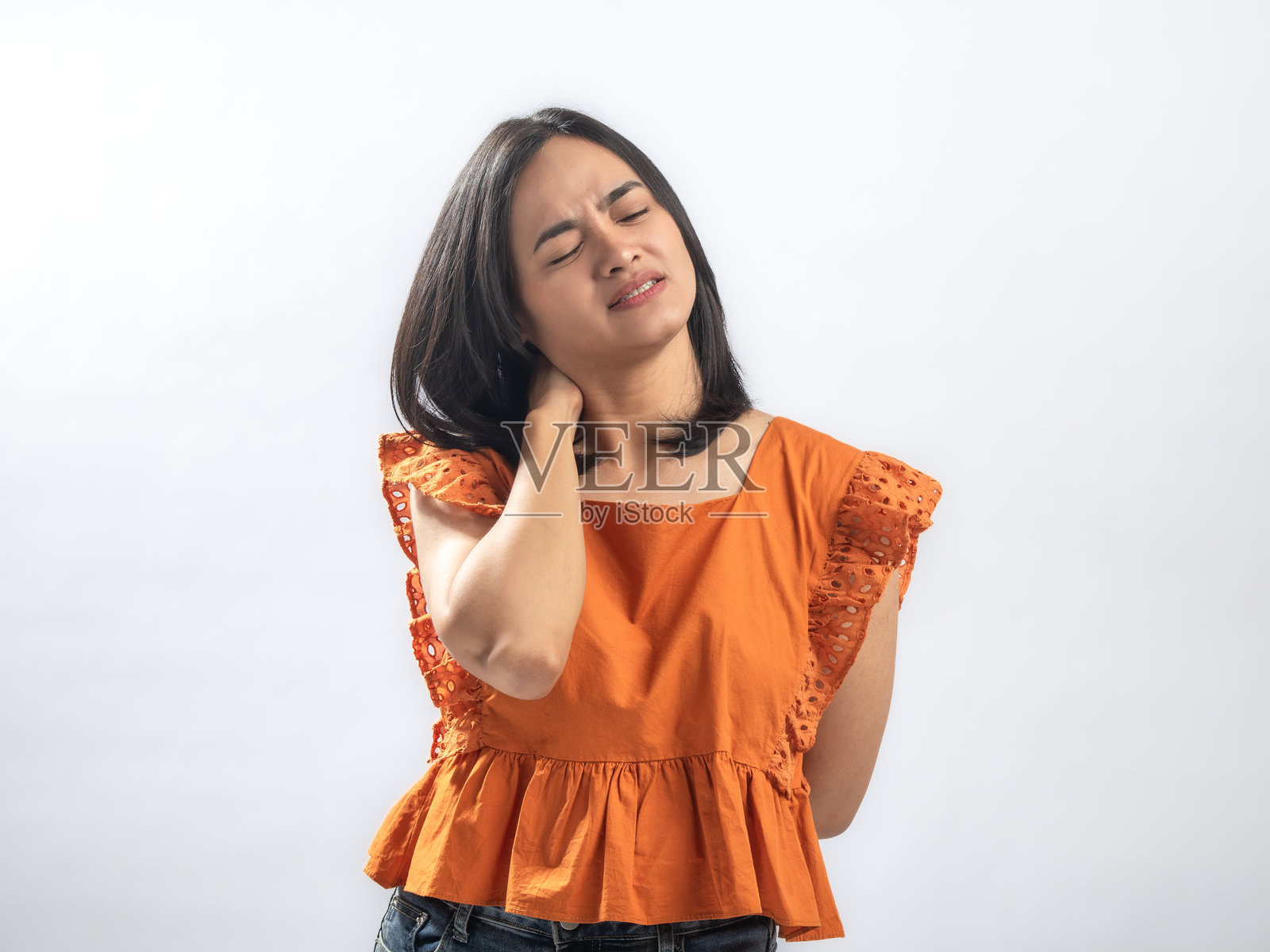 一名身穿橙色荷叶边衬衫的亚洲女性，触摸着脖子并痛苦地皱眉，表示不适或肌肉拉伤，站在纯白色背景前照片摄影图片