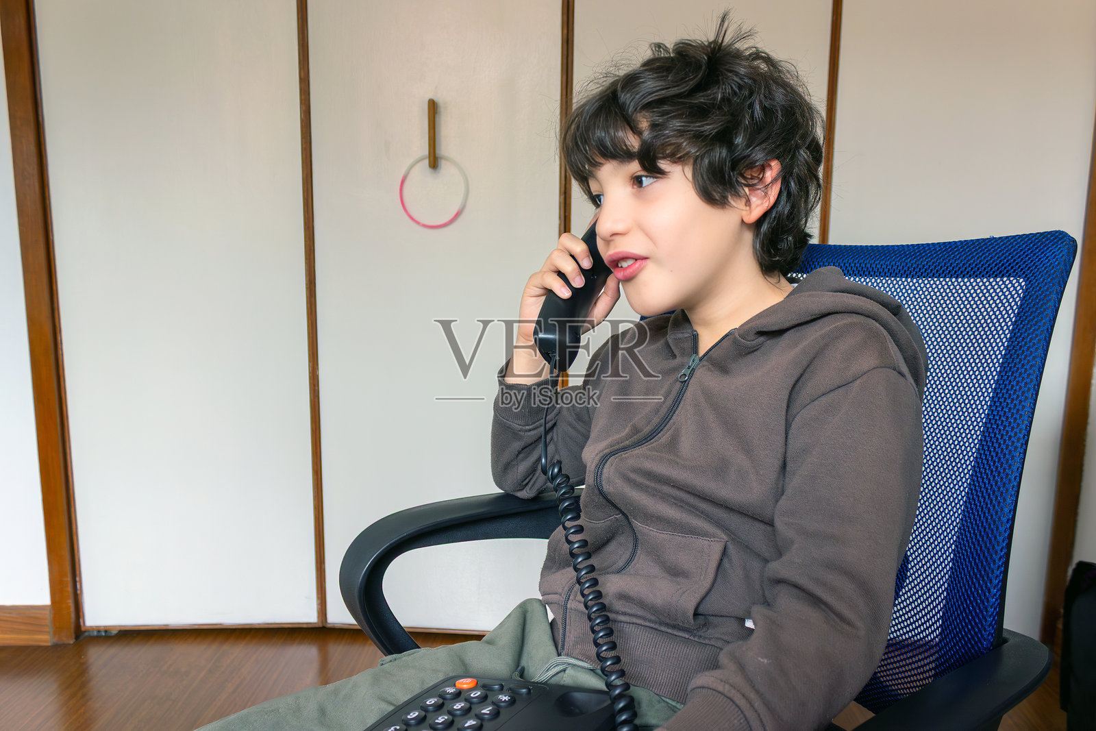 留着波浪卷发的孩子在家中对着复古电话说话和倾听，室内生活方式系列照片摄影图片