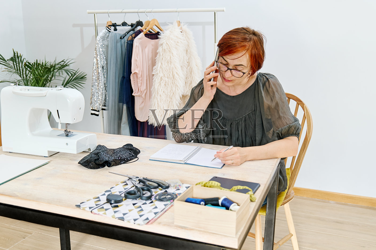 一位女性设计师在精品工作室裁缝店使用智能手机，查看客户订单照片摄影图片