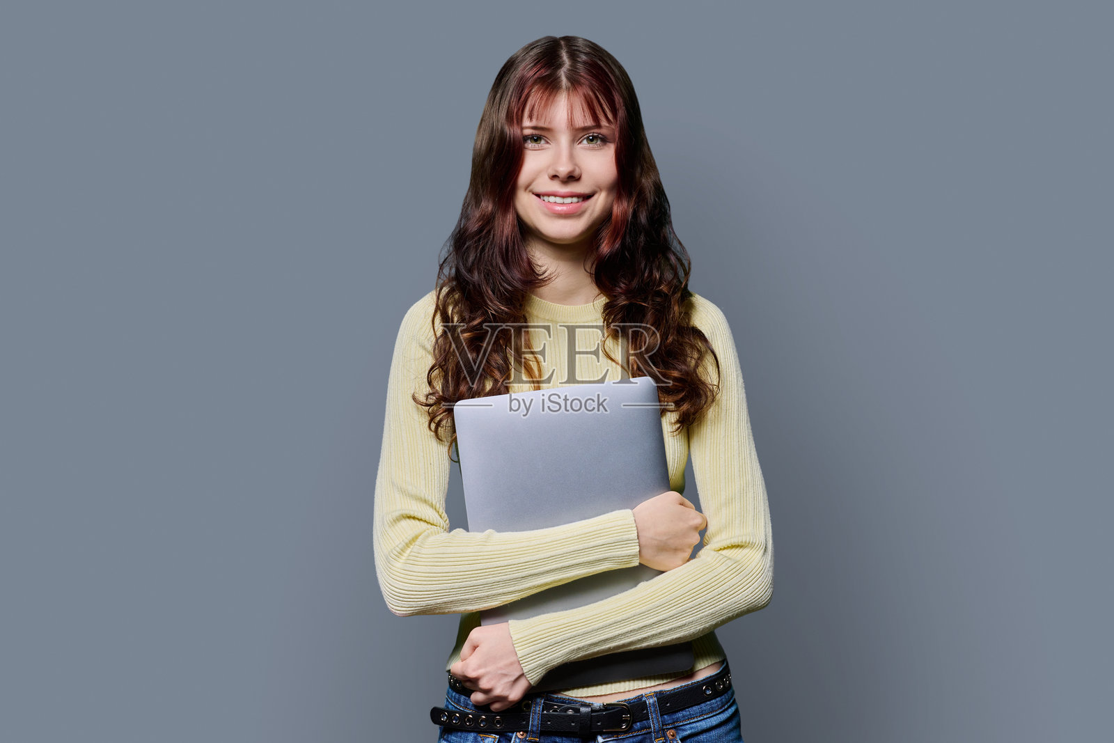 背景为灰色的漂亮女高中生肖像，手持笔记本电脑照片摄影图片