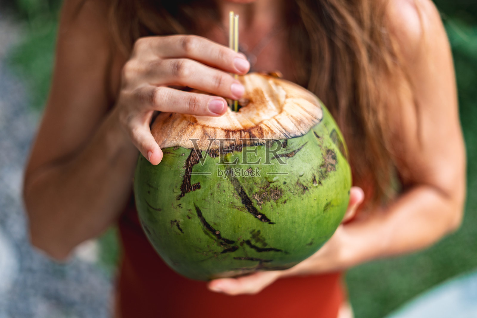 一位女士拿着一个插着吸管的绿椰子照片摄影图片