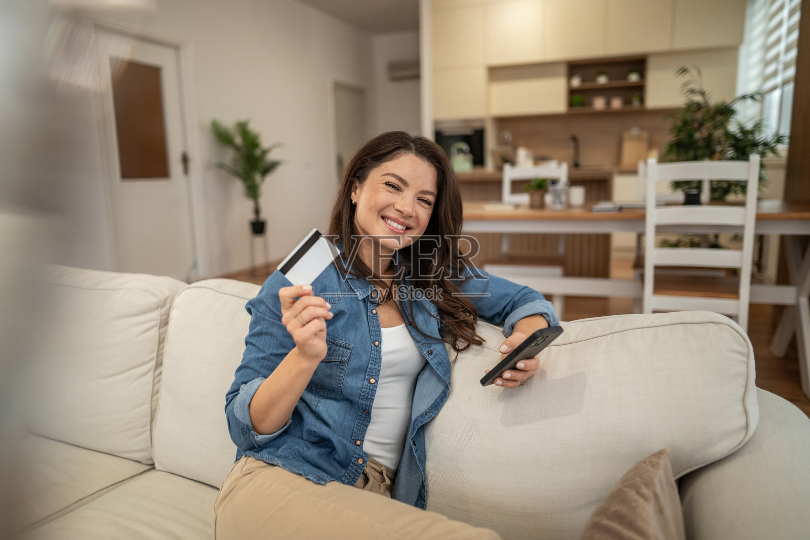 年轻女子微笑着，手持信用卡和智能手机照片摄影图片