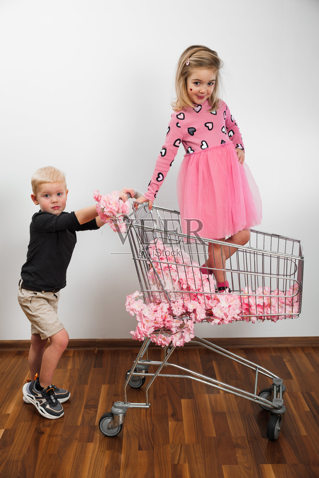 孩子们在一个房间里，推着装满粉色装饰品的购物车玩得很开心照片摄影图片
