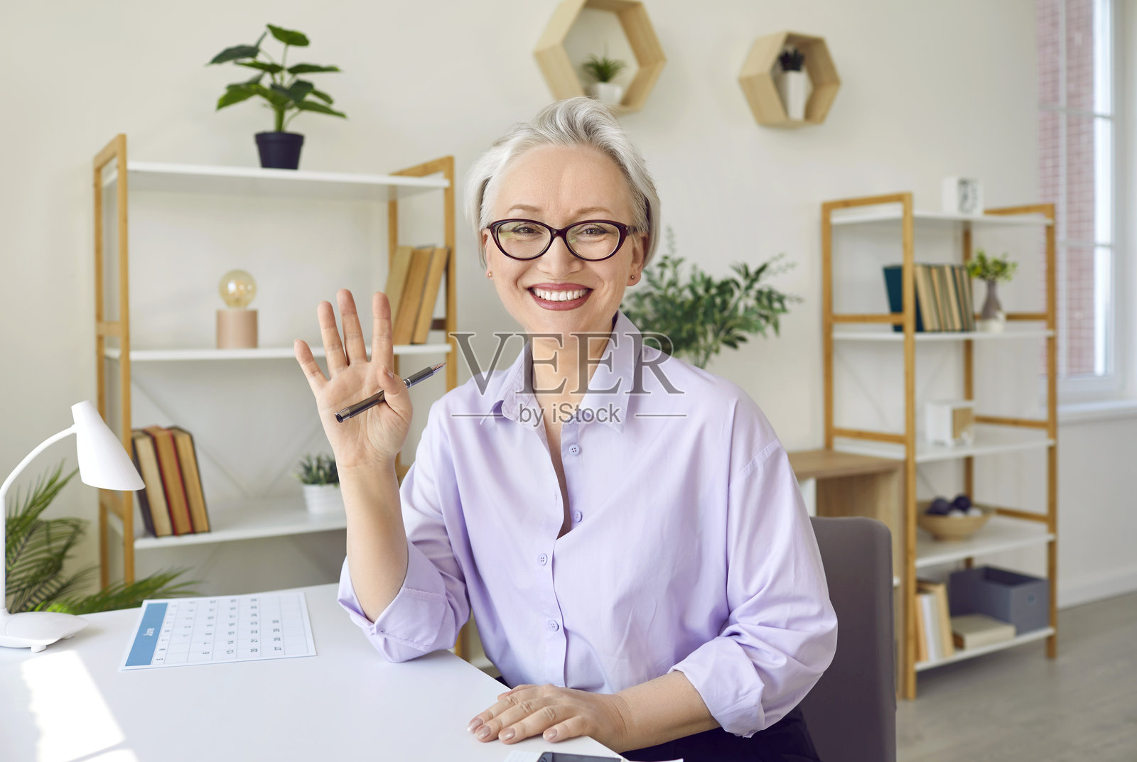 一位开心的中年女教师在虚拟视频会议中挥手致意照片摄影图片
