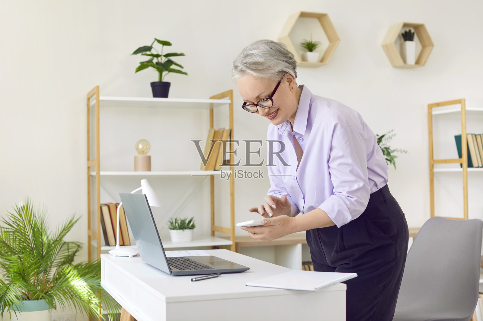 一位快乐的年长女商人正在办公室使用智能手机整理工作日程。照片摄影图片