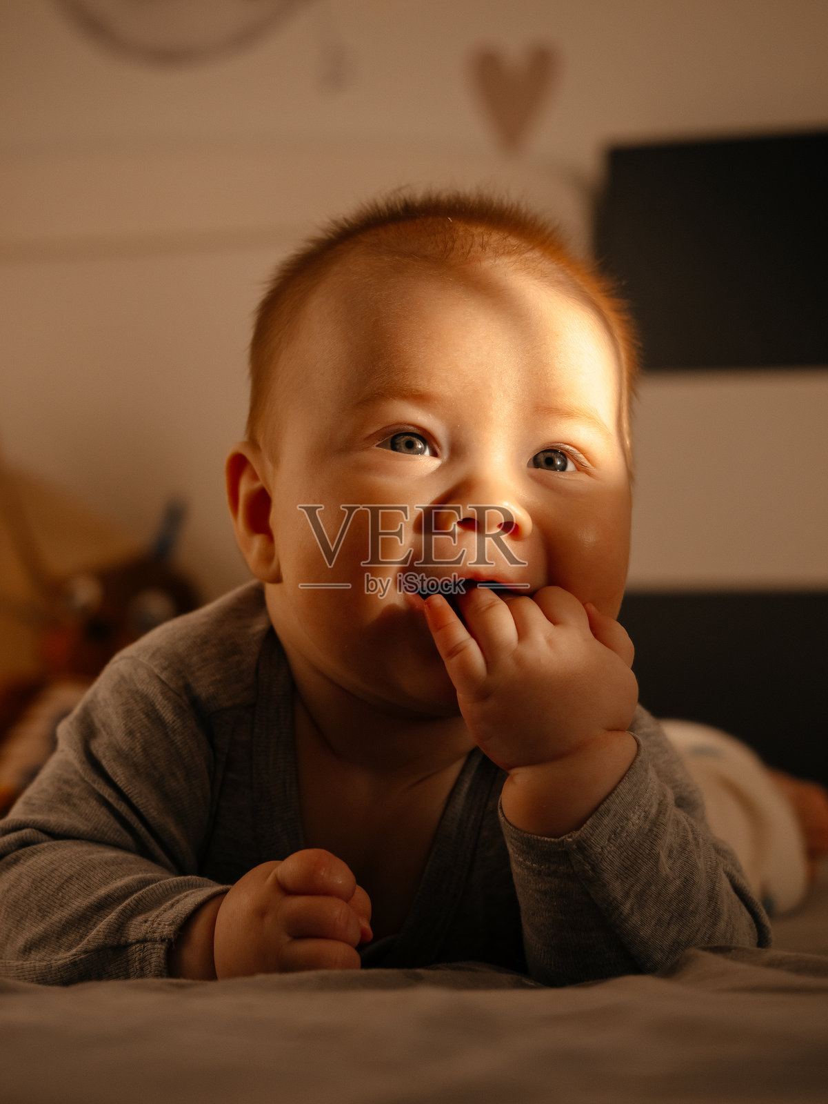 婴儿趴在卧室里，手里拿着嘴，看着镜头照片摄影图片