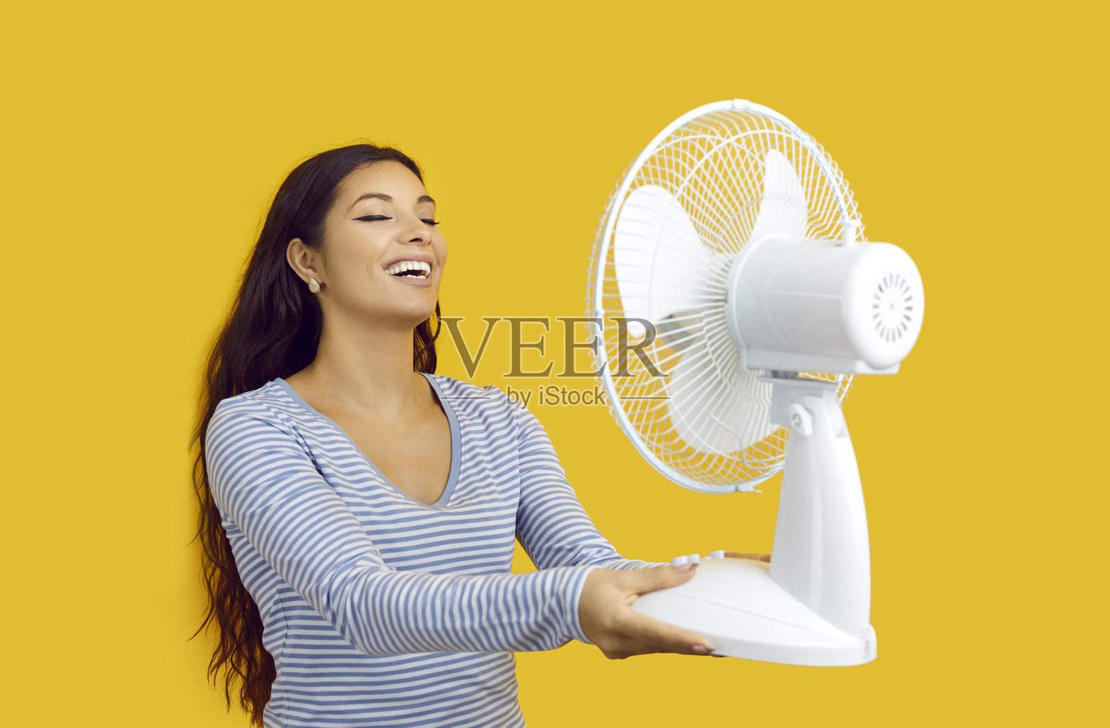 一名快乐的女子在黄色背景下享受电风扇吹来的风照片摄影图片