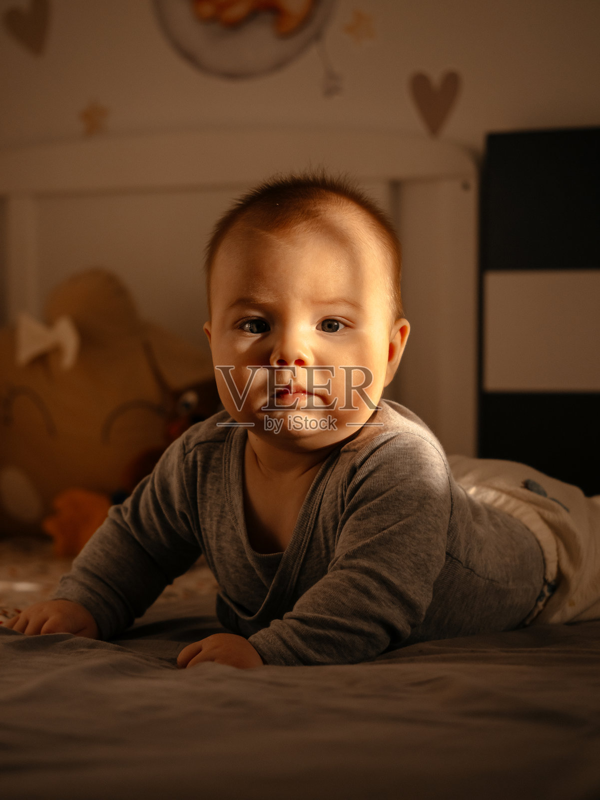 婴儿趴在床上看着镜头，背景是舒适的卧室照片摄影图片