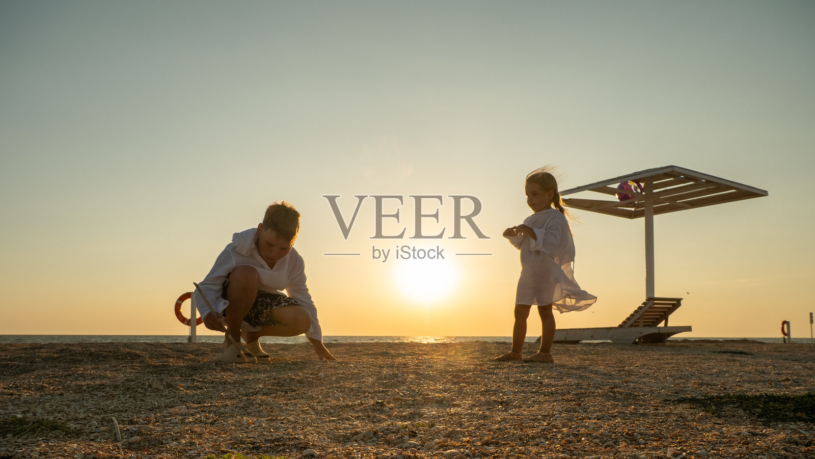 孩子们在黄金时刻探索沙滩。他们的剪影在平静的海洋上温暖的日落背景下显得格外突出，唤起了无忧无虑、宁静的家庭时光回忆。照片摄影图片