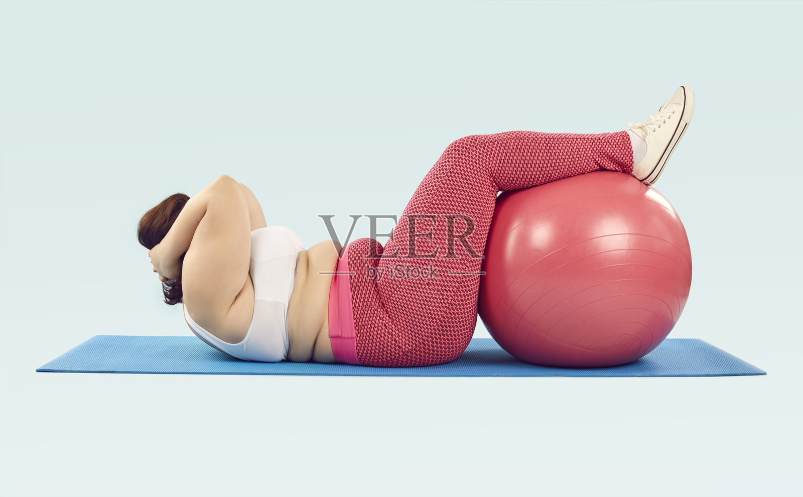 超重女性躺在运动垫上，使用瑞士球进行仰卧起坐锻炼照片摄影图片