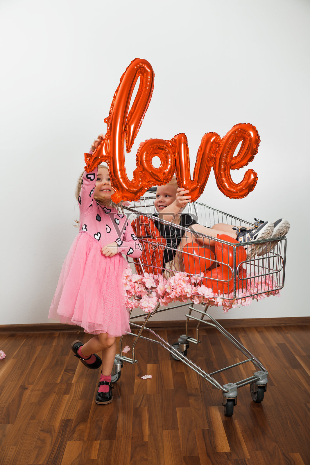 孩子们在购物车里玩耍，手举爱心标志，周围装饰缤纷多彩照片摄影图片
