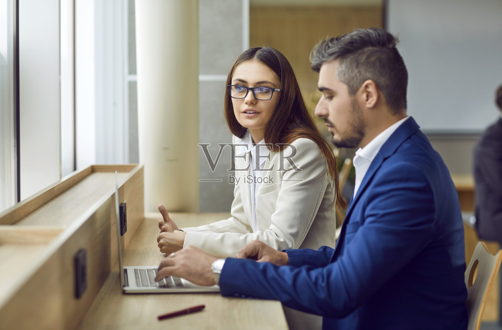 年轻女子和男子坐在办公桌旁，使用笔记本电脑并讨论事情照片摄影图片
