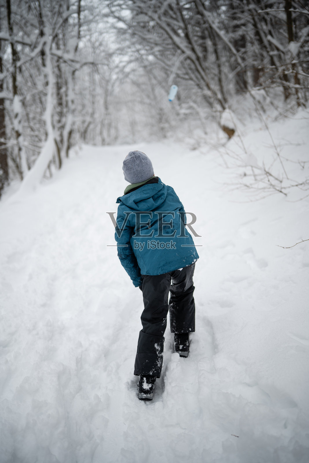 冬季森林里，一个小男孩在雪地小径上徒步照片摄影图片