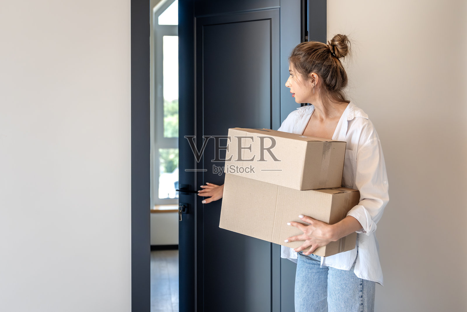 女子抱着箱子打开公寓门，如释重负。一人。照片摄影图片